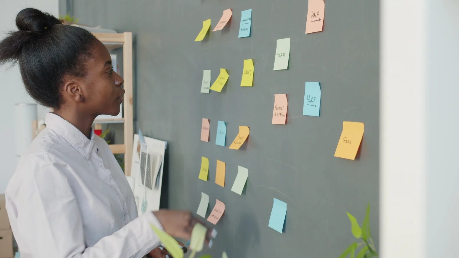 Focused young woman analyzing sticky notes on a chalkboard for project planning.